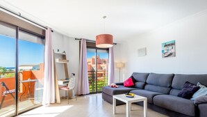 Una sala de estar moderna con un sofá gris, una mesita blanca y un balcón con puerta de cristal.