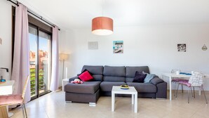 Una sala moderna con un sofá seccional gris, una mesita de noche blanca y una zona de comedor con una mesa y sillas blancas.