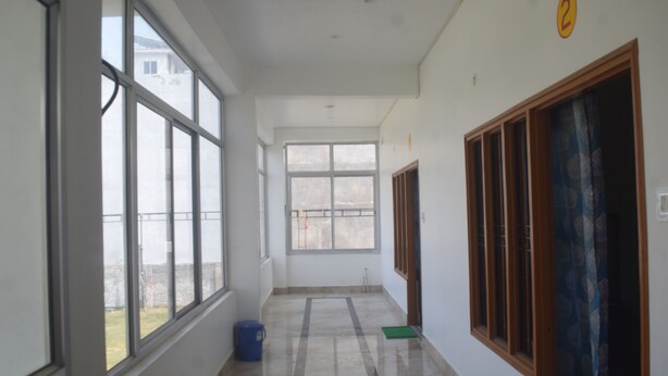 A corridor with large windows, a blue trash bin, and a green mat on the floor. - Amrit Palace (Faizabad)