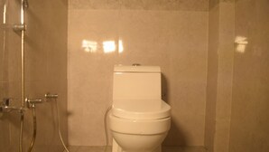A bathroom with a toilet, a shower, and a tiled floor. - Amrit Palace (Faizabad)