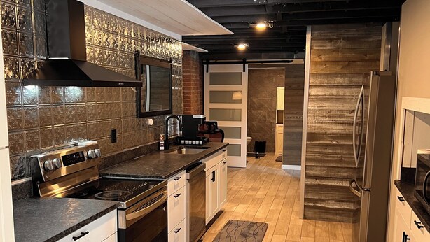 A modern kitchen with wooden flooring, stainless steel appliances, and a brick backsplash.