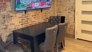 A conference room with a large flat-screen TV mounted on a brick wall, a dark wooden table, and four upholstered chairs.