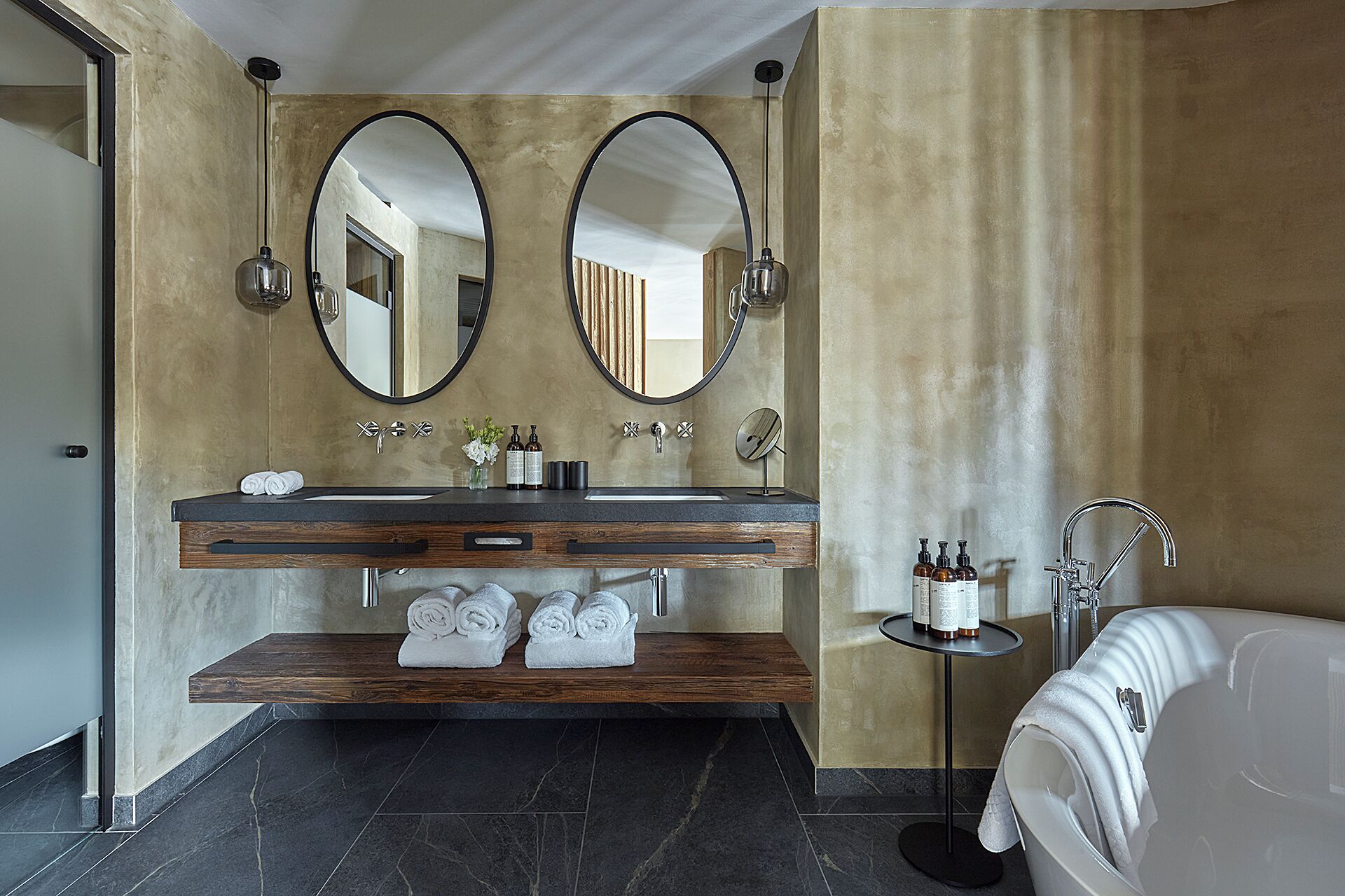 Een moderne badkamer met een dubbele wastafel, twee grote spiegels, een badkuip en een klein tafeltje met toiletartikelen.