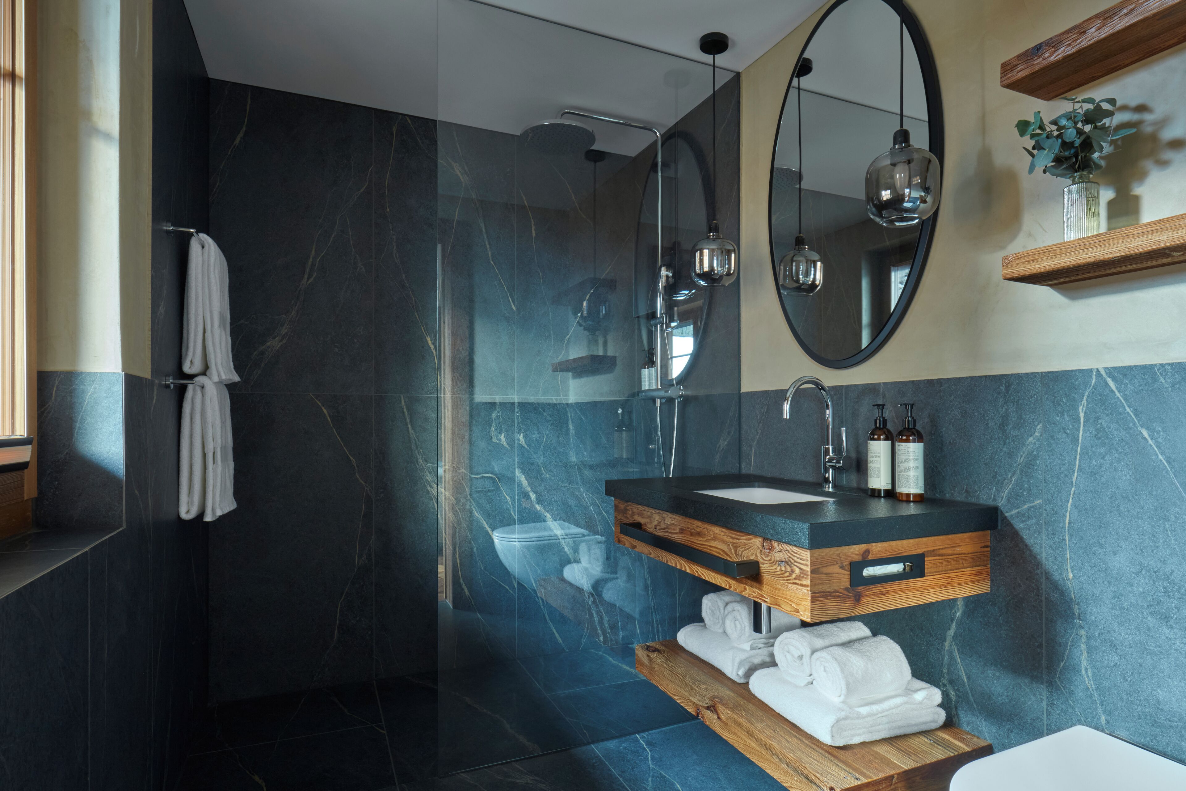 A modern bathroom with a dark marble wall, a wooden vanity with a sink, and a large mirror above the vanity.