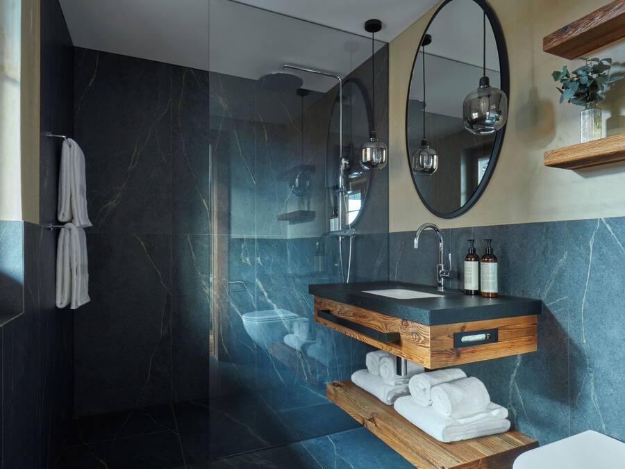 A modern bathroom with a dark marble wall, a wooden vanity with a sink, and a large mirror above the vanity.