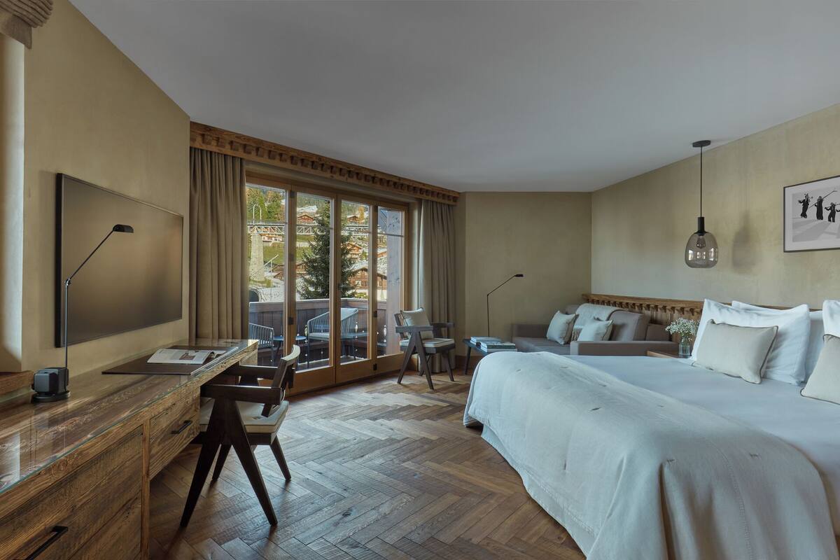 Una camera d'albergo con un letto grande, una scrivania con una sedia, una TV e una finestra vista edifici e alberi.