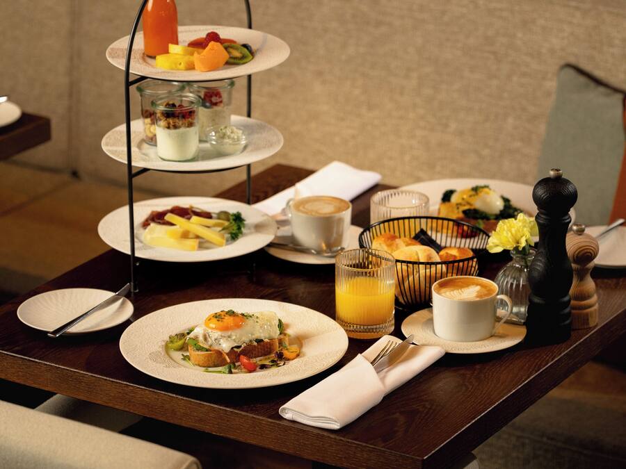 Ein Frühstückstisch mit einem dreistöckigen Serviertablett, Speisen auf Tellern, einer Kaffeetasse und einem Glas Orangensaft.