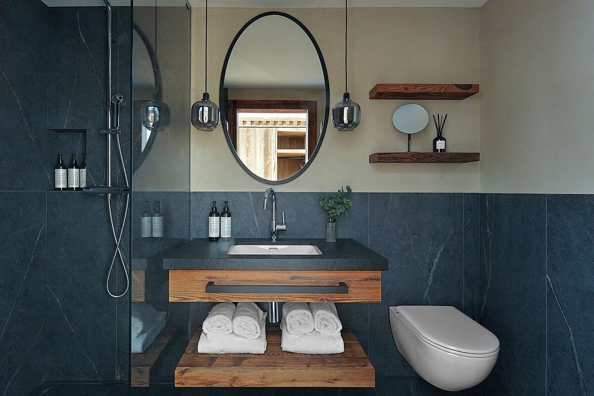A modern bathroom with a dark marble wall, a wooden vanity, a white toilet, and a shower area.