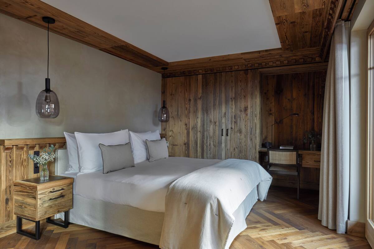 Una camera da letto con testiera in legno, un comodino in legno con cassetti, un tavolino da notte con un vaso di fiori e una scrivania con una sedia.