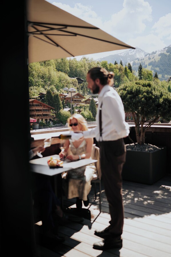 Un comedor con una mesa y sillas, una persona de pie, y una vista de un paisaje montañoso al fondo.