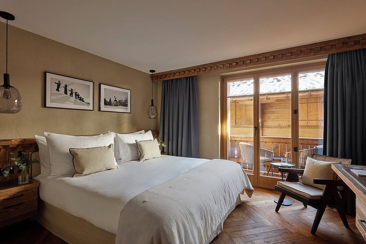 Una camera d'albergo con un letto grande, un comodino in legno, una scrivania con una sedia e vista su un pontile di legno attraverso una porta in vetro.