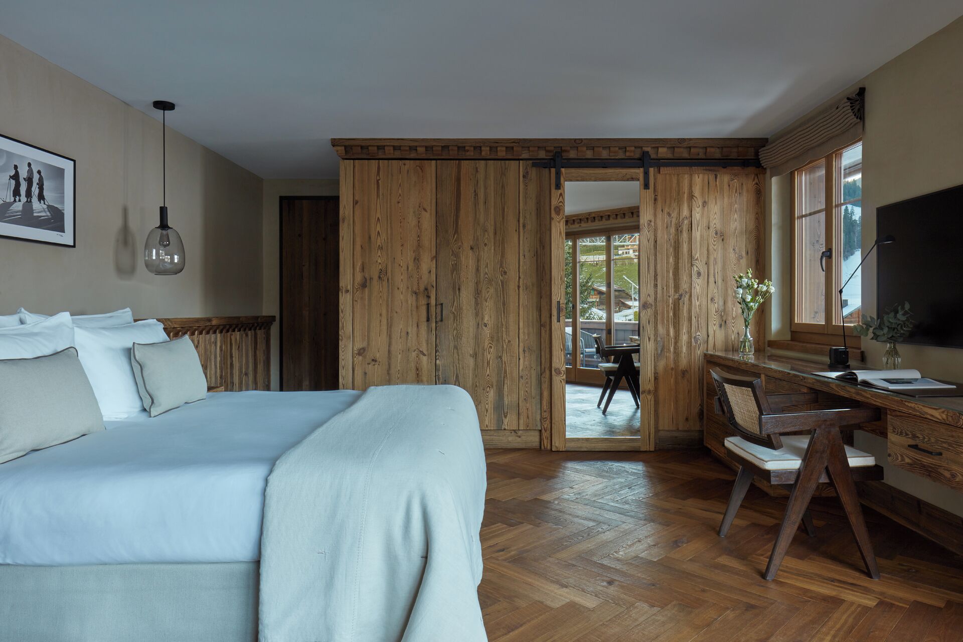 A bedroom with a bed, a desk, and a view of the outdoors.