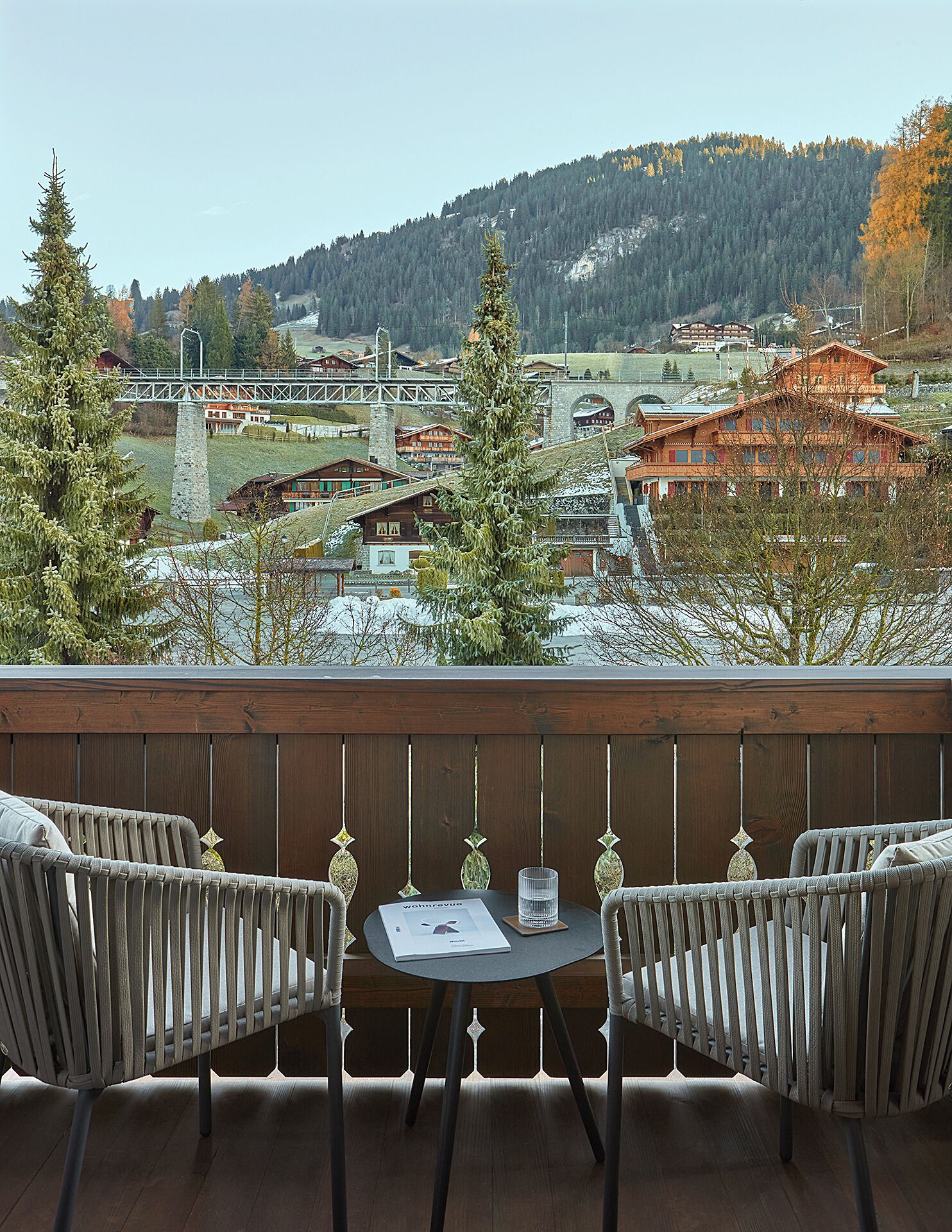 A balcony with two wicker chairs, a small table, and a glass of water.