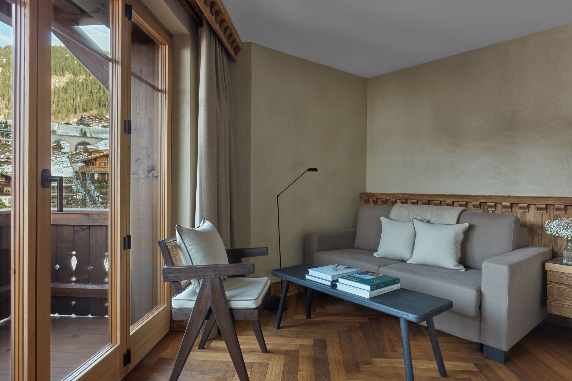 Una sala de estar acogedora con piso de madera, un sofá, una silla y una mesa con libros.