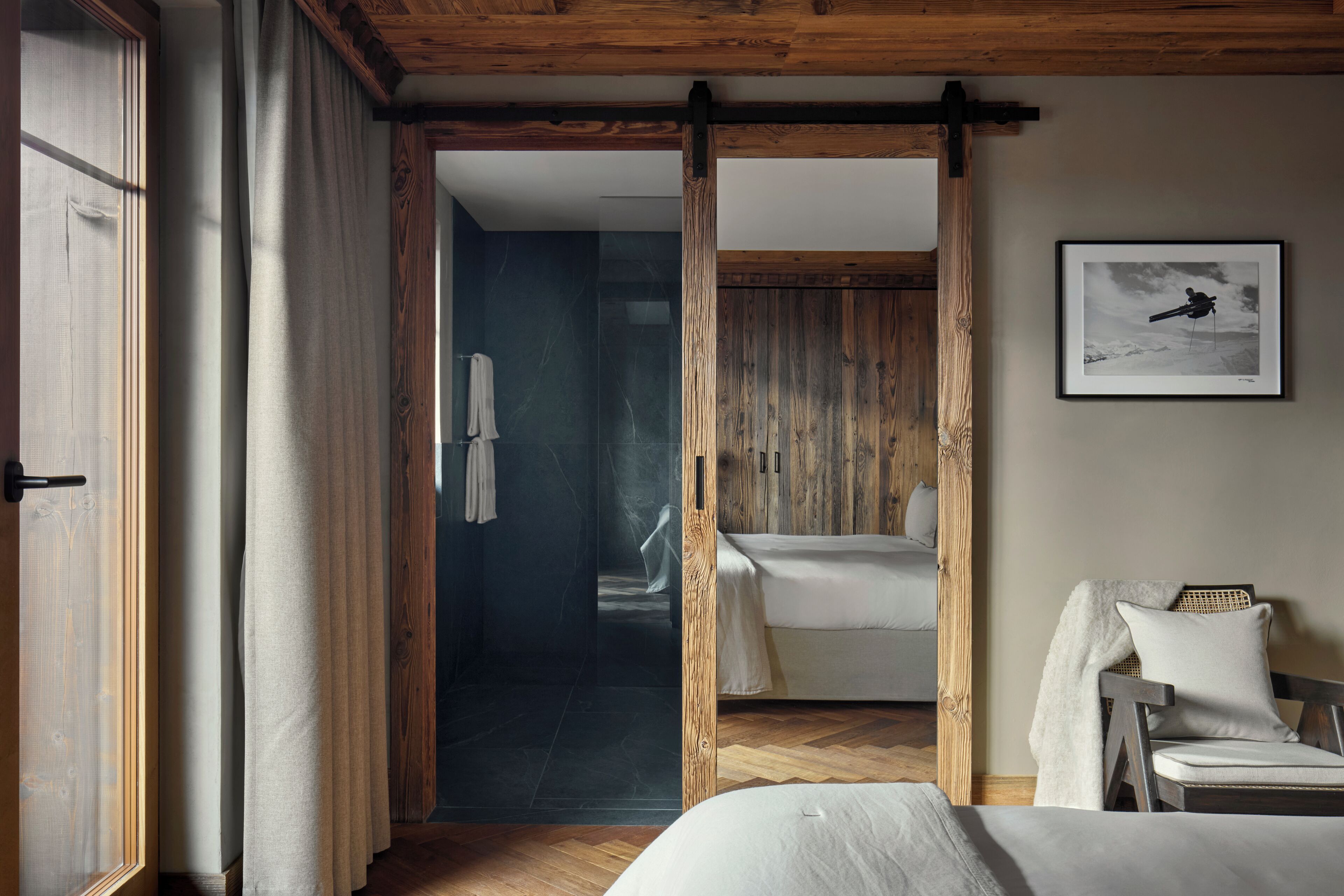 A bedroom with a wooden ceiling, a bed, a chair, and a framed picture on the wall.