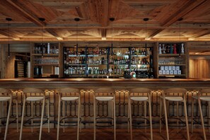 A bar with wooden ceiling and shelves stocked with bottles and glasses. There are bar stools and a counter.