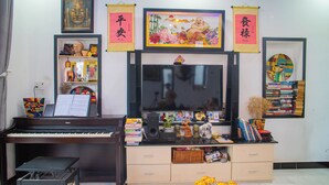 A living room with a piano, a television, and various decorative items including books and framed pictures on the walls. - Sophia Homestay Hoi An (Da Nang)