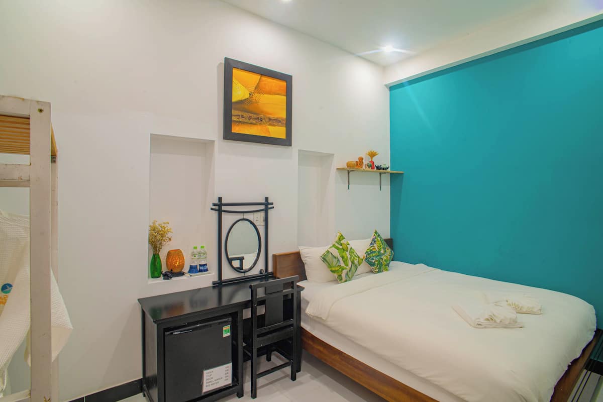 A hotel room with a bed, a desk, a chair, a mirror, and a wall with a painting.