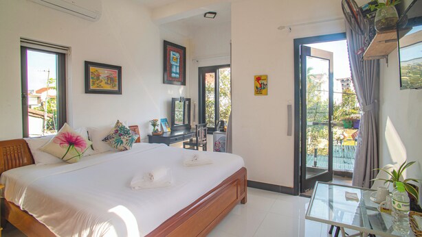 A hotel room with a large bed, a desk, and a balcony with a view. - Sophia Homestay Hoi An (Da Nang)