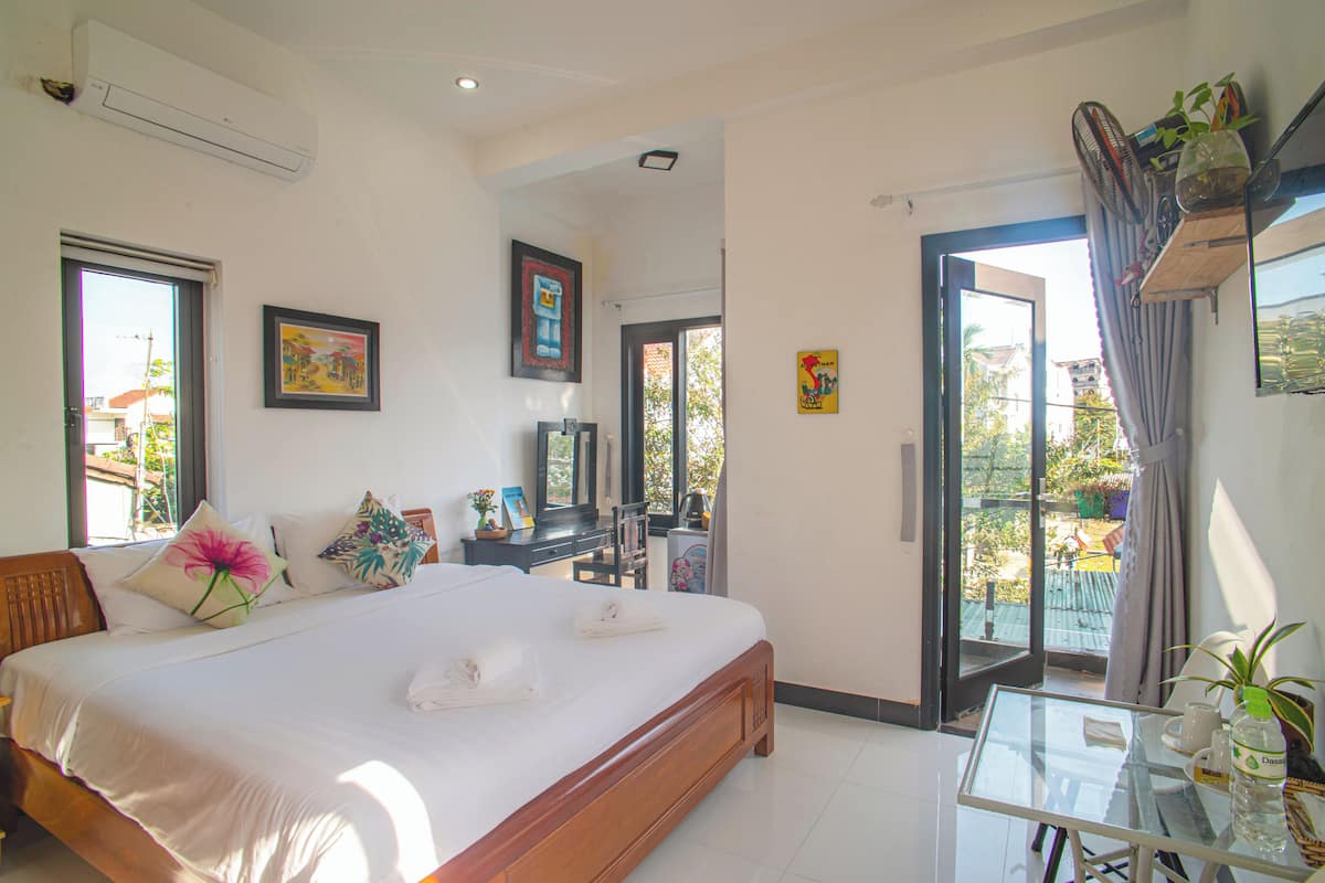 A hotel room with a large bed, a desk, and a balcony with a view.