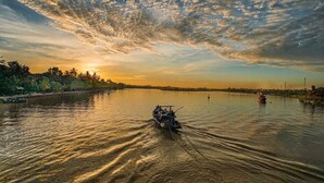 A calm river at sunset with a small boat in the foreground. - Sophia Homestay Hoi An (Da Nang)