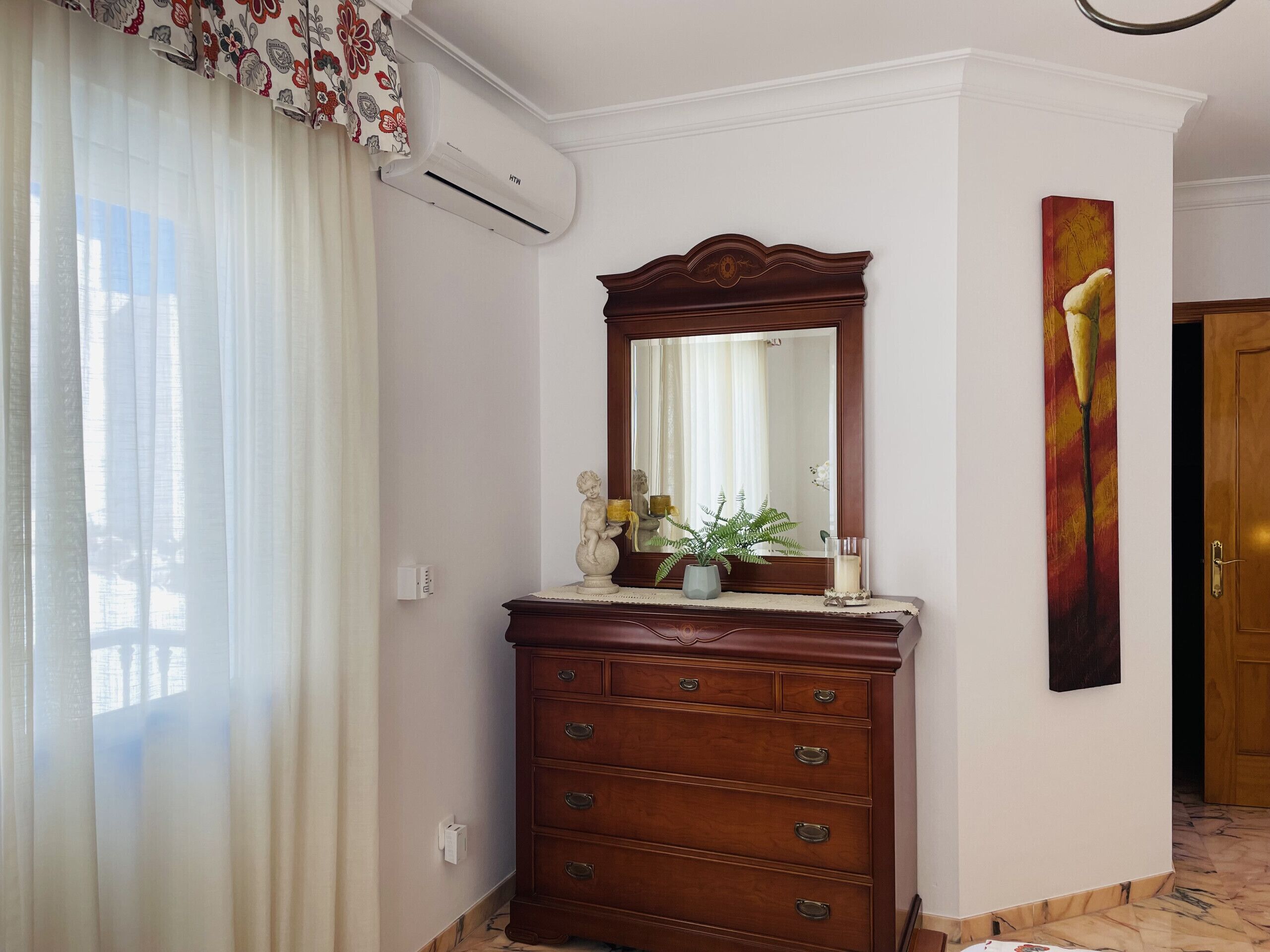 Une commode en bois avec un miroir, une plante en pot et un vase avec une bougie.