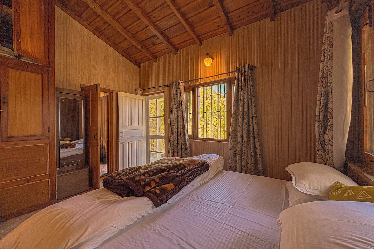 Une chambre avec deux lits, des murs en bois, une armoire et une fenêtre avec des rideaux.
