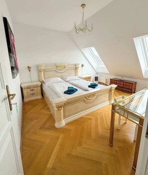 Ein Schlafzimmer mit einem großen Bett, einer Kandelaber, Holzboden und Blick zum Himmel durch die geneigte Decke.
