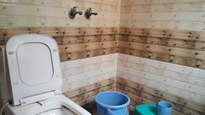 A small, compact bathroom with a white toilet, a blue bucket, and a green container. - Hotel Indigo (Rohtak)