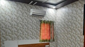 A bedroom with a bed, a wooden headboard, a wall-mounted air conditioner, and patterned wallpaper. - Hotel Indigo (Rohtak)