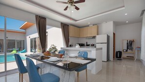 A modern kitchen with a central island, blue chairs, and a view of a swimming pool. - Andaman Sea Best Pool Access & Villas   (Chalong)