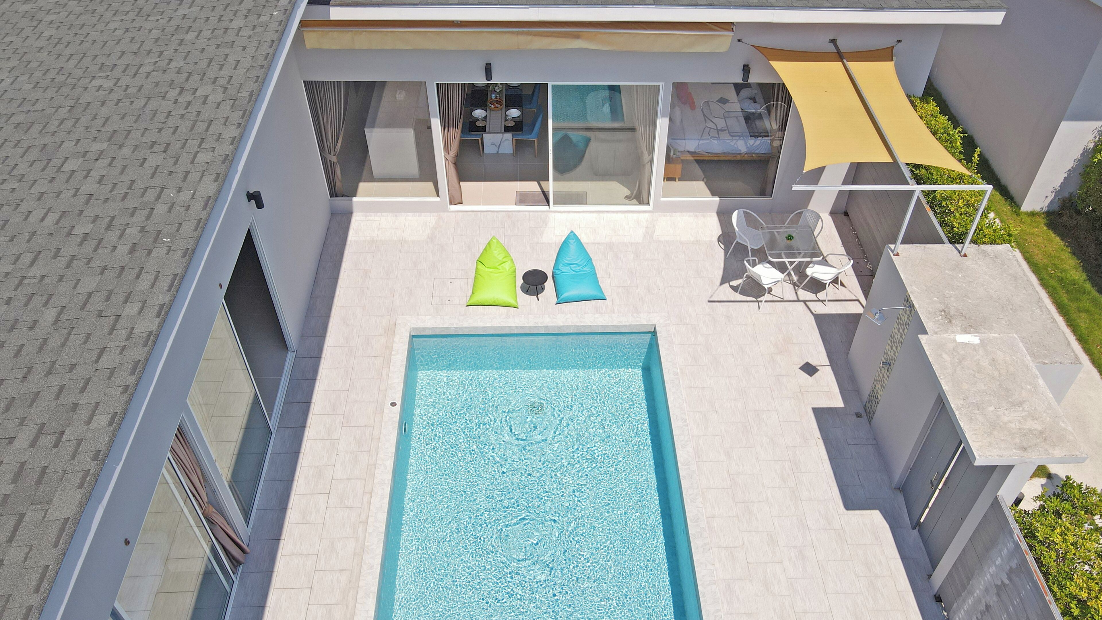 An aerial view of a modern house with a swimming pool, a dining area, and a covered patio.