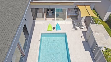 An aerial view of a modern house with a swimming pool, a dining area, and a covered patio.