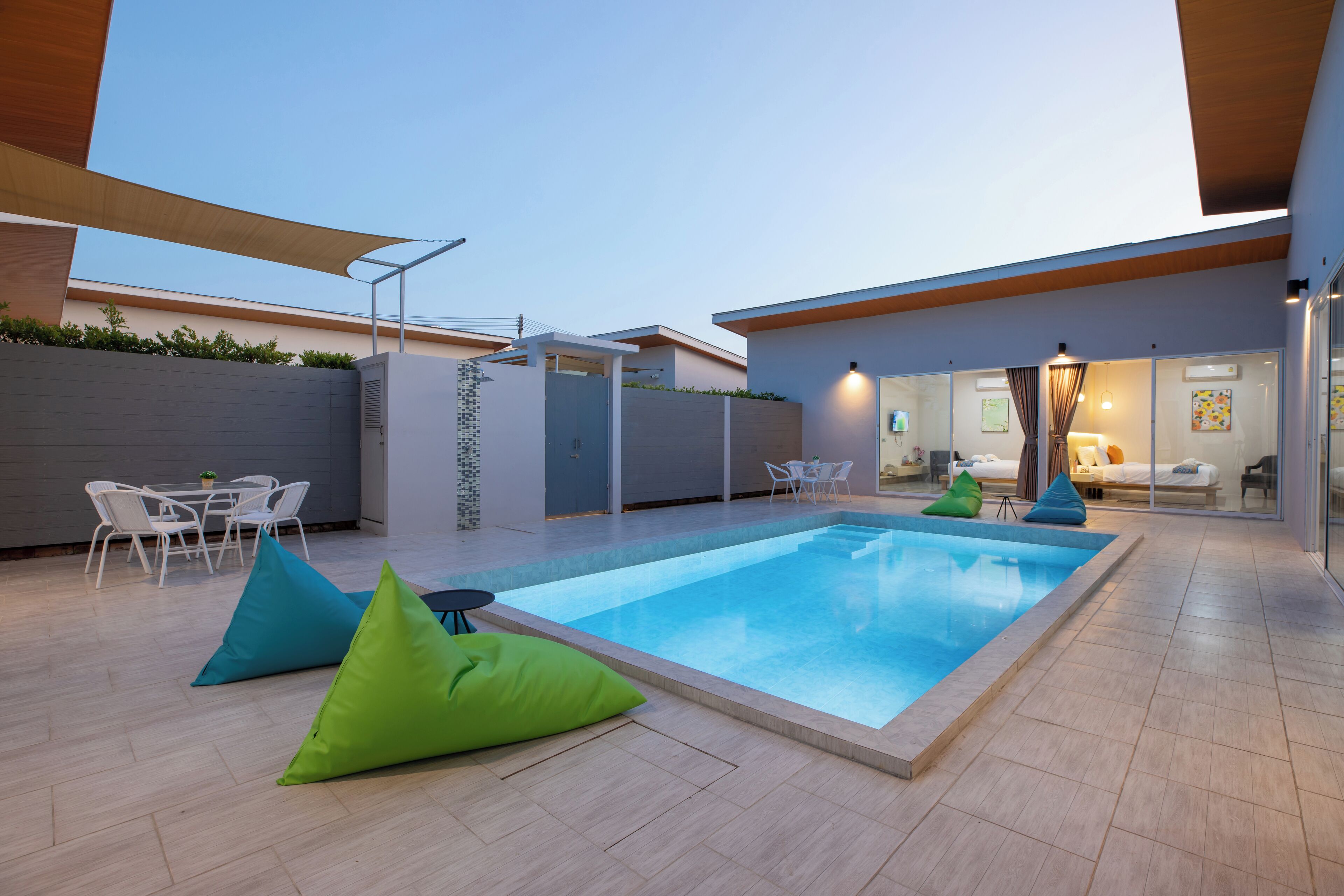 A modern outdoor pool area with a clear blue pool, white outdoor furniture, and a wooden deck.