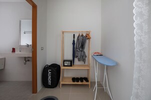 A bathroom with a wooden drying rack, a blue ironing board, and a black laundry bag.