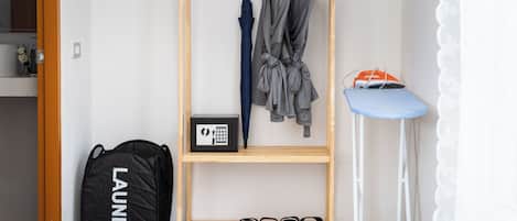 A wooden wardrobe with hanging clothes, a blue stool, and a black laundry bag.