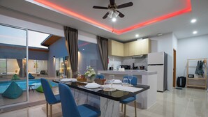 A modern kitchen with a central island, a dining area with blue chairs, and a visible pool area. - Andaman Sea Best Pool Access & Villas   (Chalong)