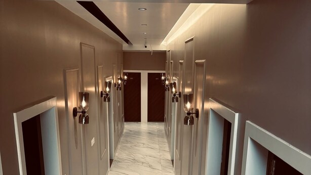 A modern hallway with marble flooring, recessed lighting, and doors with wall-mounted sconces. - Hotel Meritus Mount Abu (Abu Road)