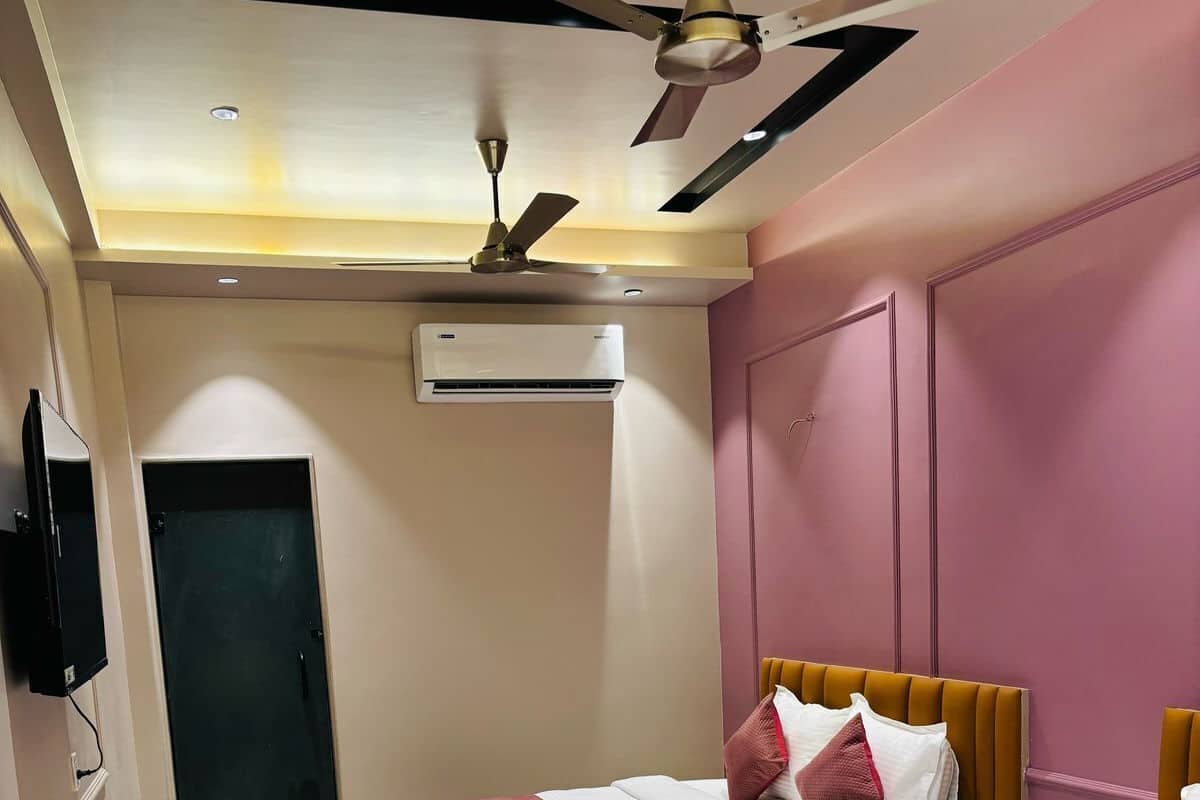 Habitación de hotel con dos camas, ventilador de techo, aire acondicionado, televisor y una puerta.