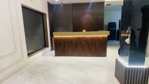 A reception area with a marble floor, a wooden reception desk, and a large black decorative piece. - Hotel Meritus Mount Abu (Abu Road)