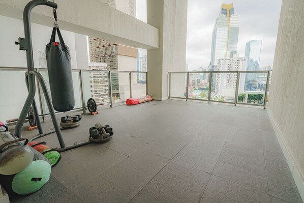 A spacious balcony with a view of a city skyline, equipped with a punching bag, dumbbells, and a weight bench.