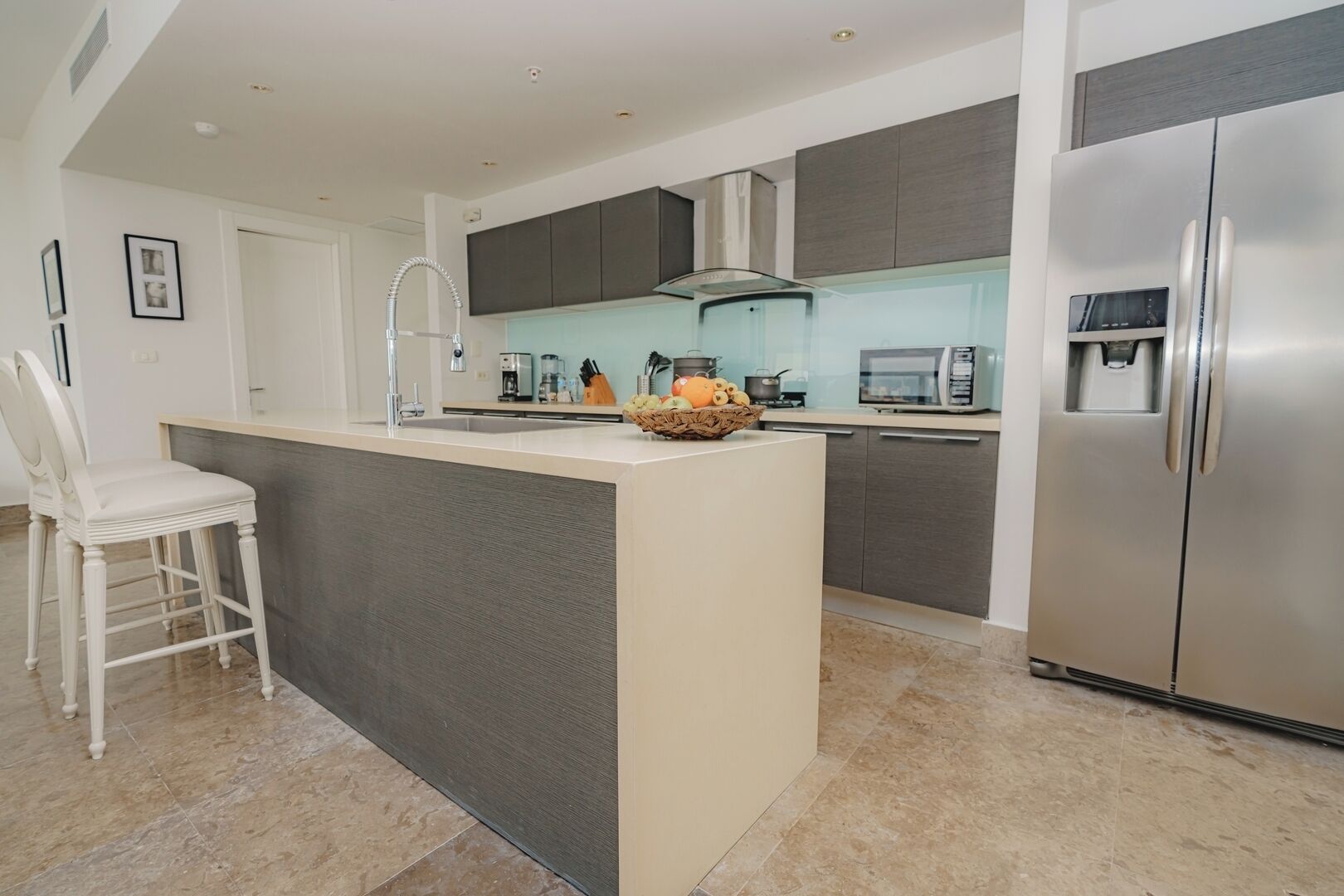 A modern kitchen with a central island, stainless steel appliances, and a white chair.