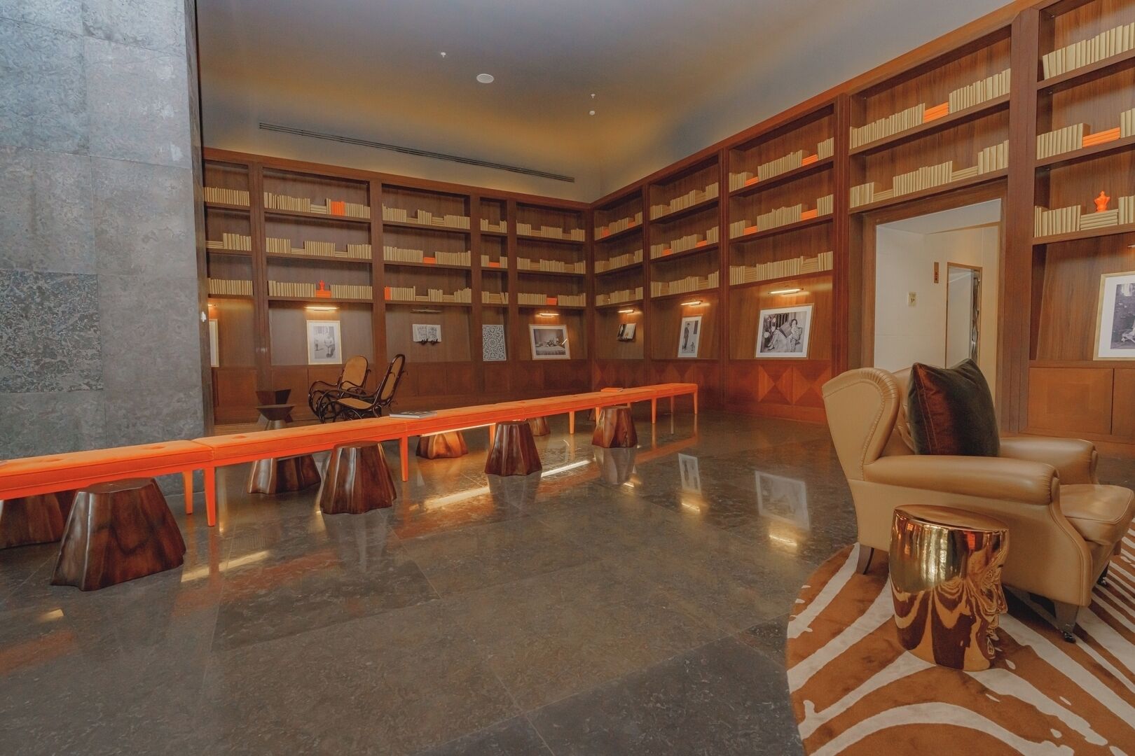 Une bibliothèque avec des étagères, un long banc en bois, un canapé et un tapis à motifs.