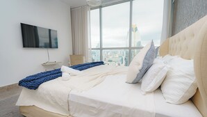 Une chambre d’hôtel moderne avec un grand lit, un téléviseur à écran plat fixé au mur et une vue sur la ville par la fenêtre.