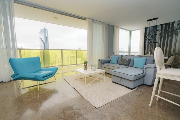 A modern living room with a blue chair, grey sofa, and a white coffee table. - Exclusive and luxury 1BR with balcony in Yoo Panama (Panamá)