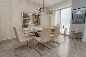 Un espace repas moderne avec une table en verre, des chaises de couleur beige et une vue sur la ville grâce à de grandes fenêtres.