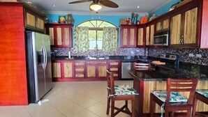 Une cuisine avec des meubles en bois, un îlot central, un ventilateur de plafond et un pare-feu en carreaux.