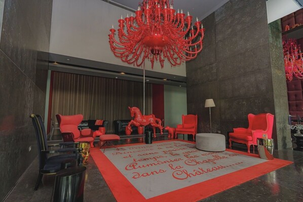 A modern lobby with red chairs, a large red chandelier, and a red horse sculpture.
