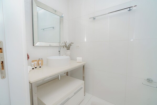 Un baño moderno con lavamanos, espejo y ducha blancos.
