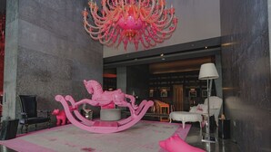 Un hall d’entrée avec un cheval à bascule rose, un lustre et un canapé blanc.